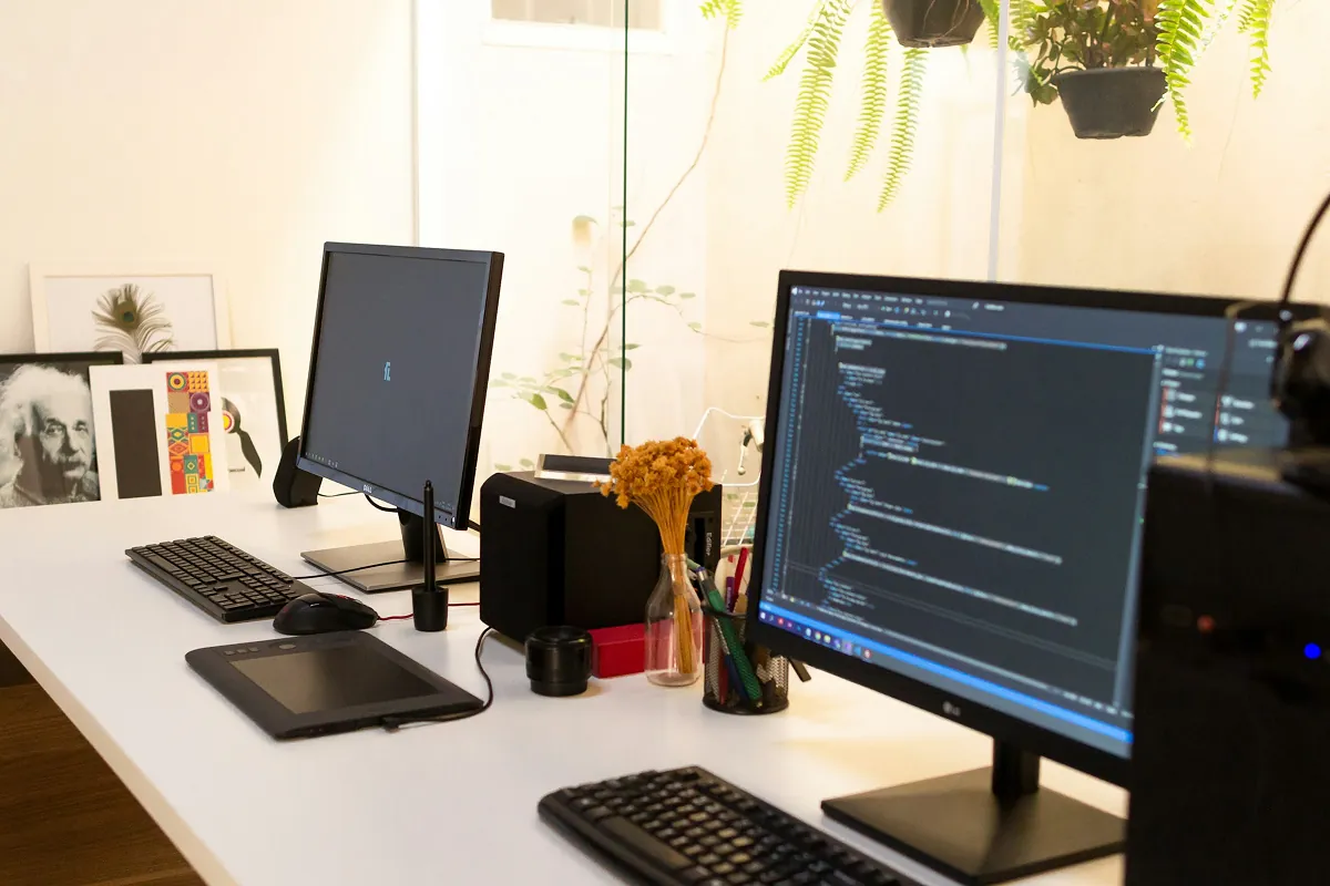 Desk with two monitors, one showing a code editor, plus a keyboard, graphics tablet and plants