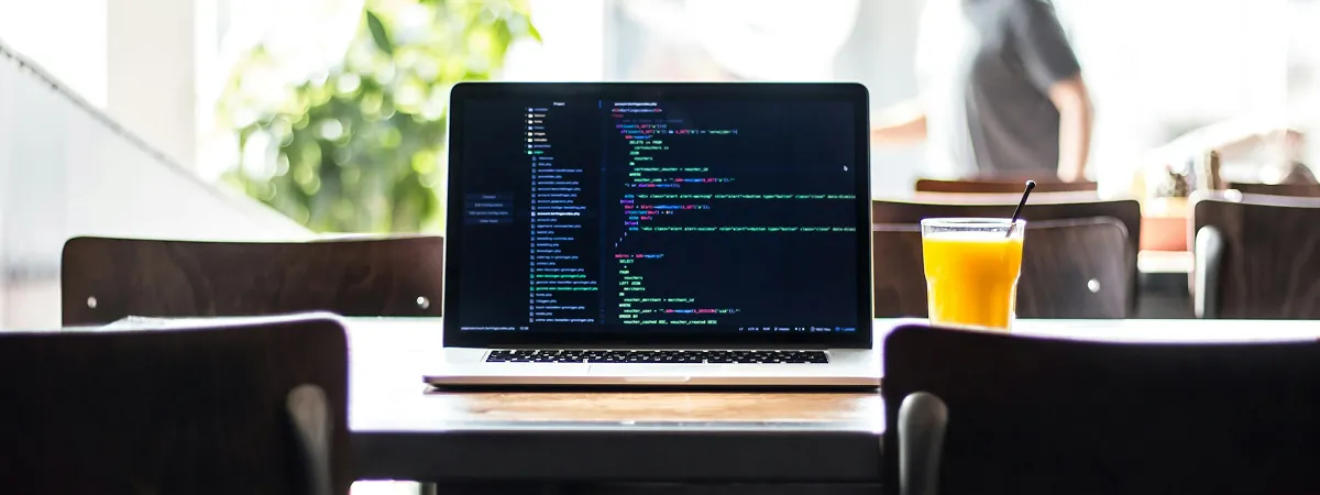 Laptop showing code on a cafe table beside a glass of orange juice