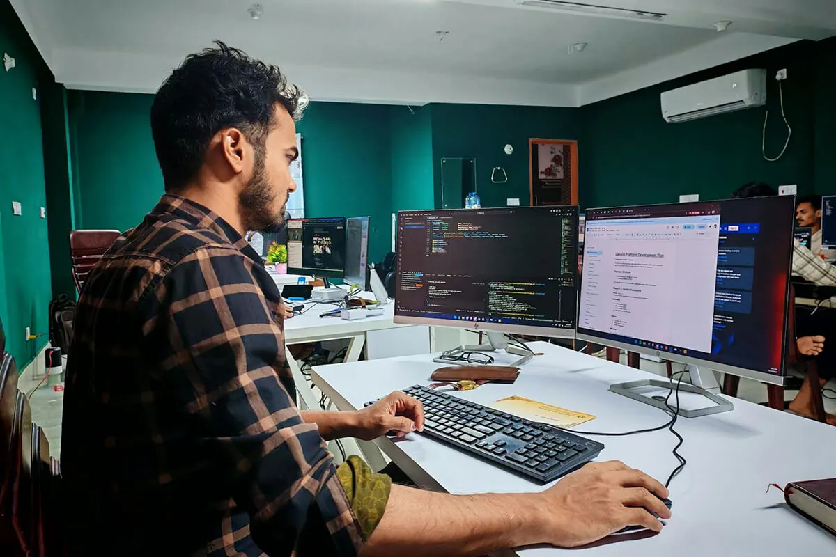 Developer at a two-monitor desk setup reviewing code alongside a project plan document