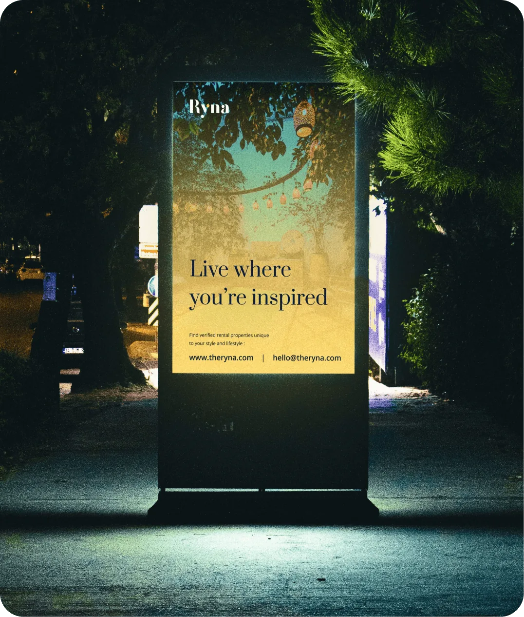 A lit Ryna street billboard at night reading “Live where you’re inspired”